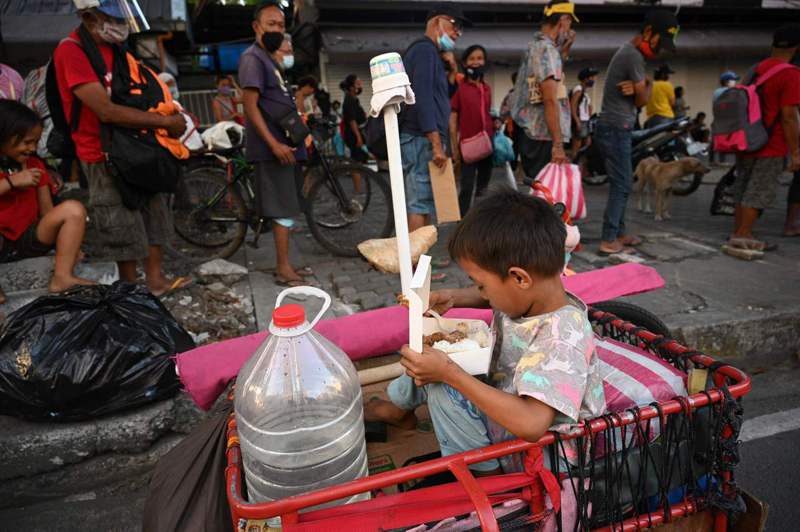 防疫封鎖措施重創菲國經濟，圖為11月24日一名菲律賓孩童坐在三輪車上吃著發放的免費便當。法新社