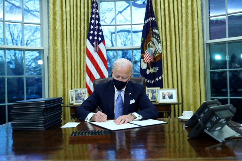 美國總統拜登20日就職當天戴著口罩在橢圓辦公室簽署行政命令。路透