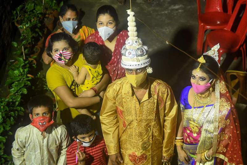 疫情下印度民眾緊縮消費，連婚姻大事都延後。圖為加爾各答封城期間，一對新人跟戴著口罩的親戚等待參加婚禮。法新社