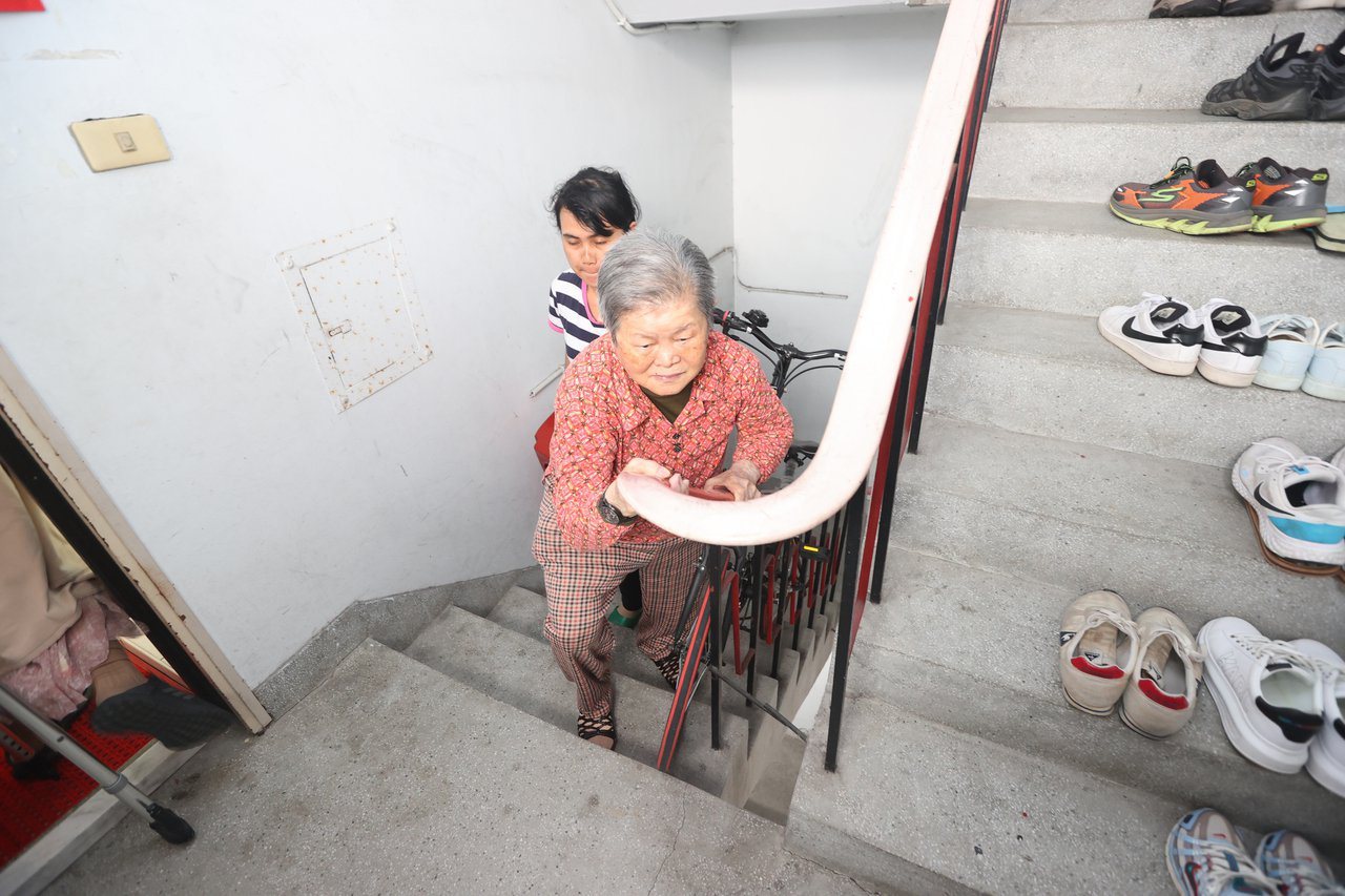 肢體不便的老母親，就醫最大障礙就是自家樓梯，必須慢慢扶著樓梯把手，一步一步地走；外籍看護則在一旁拿著椅子，讓她累時就能坐著休息。記者陳正興／攝影