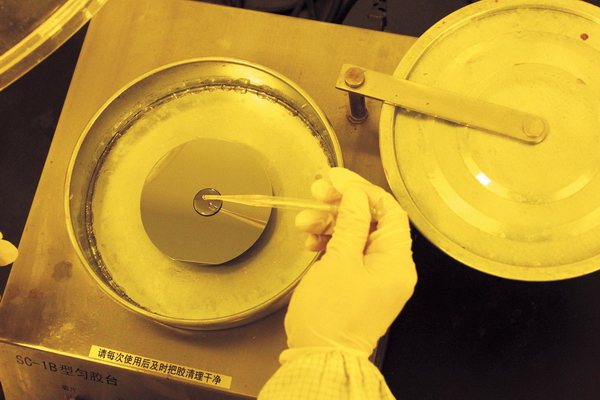 工作人員在黃色光源工作環境中把光刻膠塗在矽片上。（神州學人雜誌）