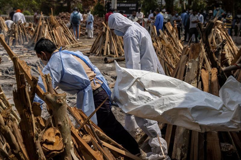 印度染疫死亡人數在28日突破20萬大關，圖為當日新德里一處火葬場工作人員抬著一具遺體準備進行火化。 法新社