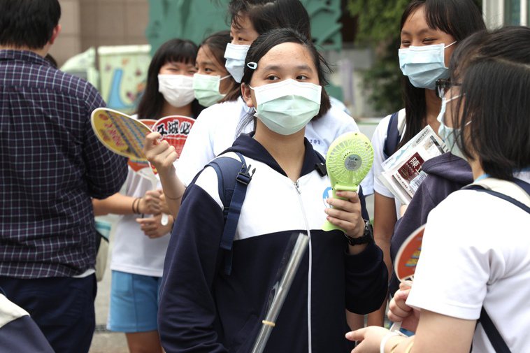 國中會考今登場，昨天考生戴起口罩手持電風扇，在炎熱的天氣和疫情威脅下看考場。記者...
