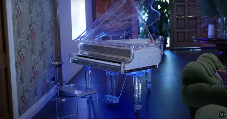 接待廳裡放著一架透明的鋼琴和遊戲機台，Cara自曝平常一個人在家會裸體彈琴。圖／摘自Youtube