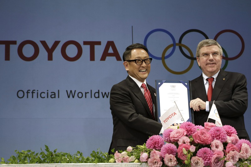 2015年豐田汽車社長豐田章男（左）與IOC主席巴赫共同舉行記者會，宣布成為最高等級的贊助企業。6年後豐田章男表示不會出席東奧開幕式。美聯社