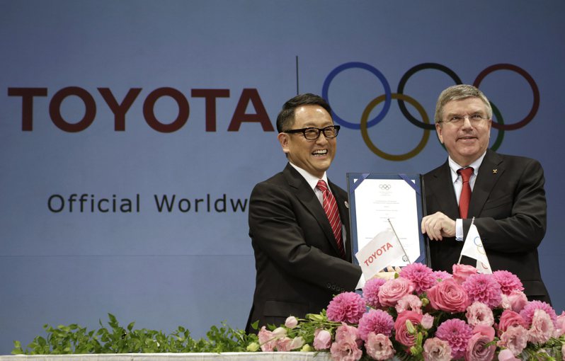 2015年豐田汽車社長豐田章男（左）與IOC主席巴赫共同舉行記者會，宣布成為最高等級的贊助企業。6年後豐田章男表示不會出席東奧開幕式。美聯社