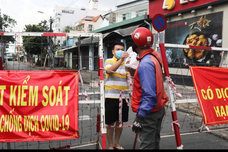 越南的胡志明市自周一起，每天下午6時到次日上午6時實施宵禁，以遏阻疫情蔓延。圖為住封鎖區的民眾透過拒馬收取食物。路透