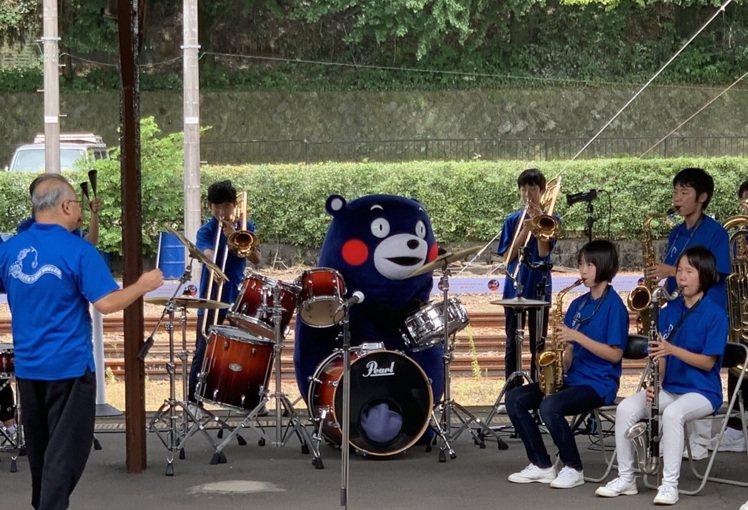擅長體操的熊本熊挑戰自我，在熊本縣人吉站與學生一起表演樂器。圖／取自Twitte...