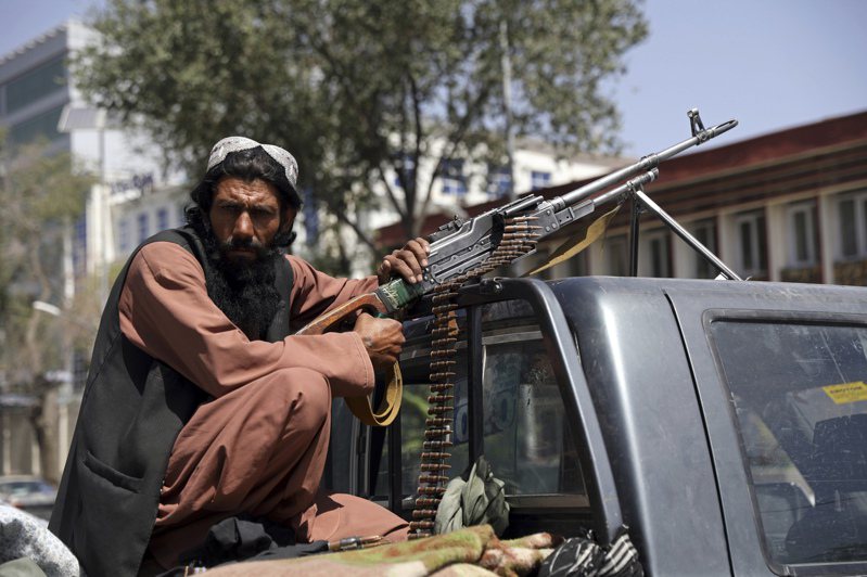 阿富汗首都喀布爾淪陷後，一名塔利班戰士神情嚴肅蹲坐在一輛帶有機槍的車輛後方。美聯社