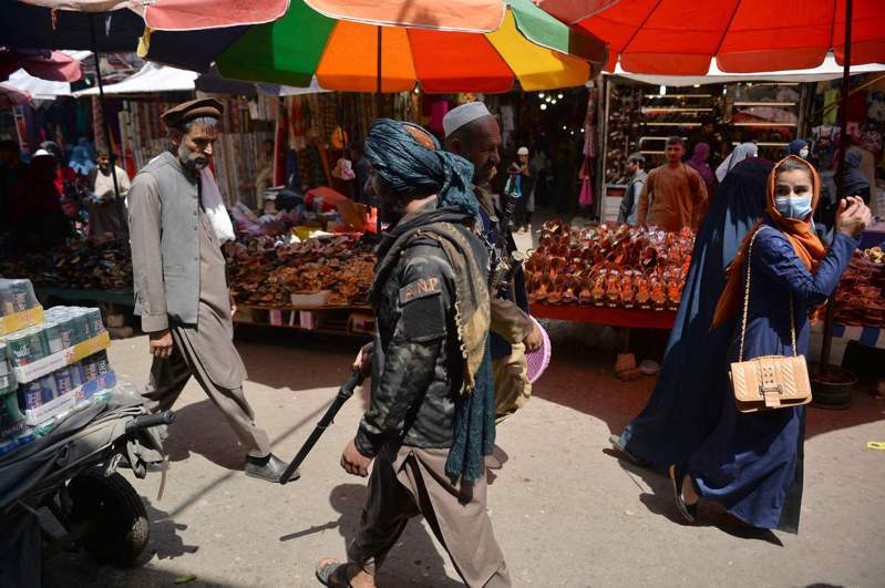 歷時20年的阿富汗戰爭宣告結束。圖為持槍的神學士民兵一日行經喀布爾一處市場，一名女子回頭看了他們一眼。（法新社）