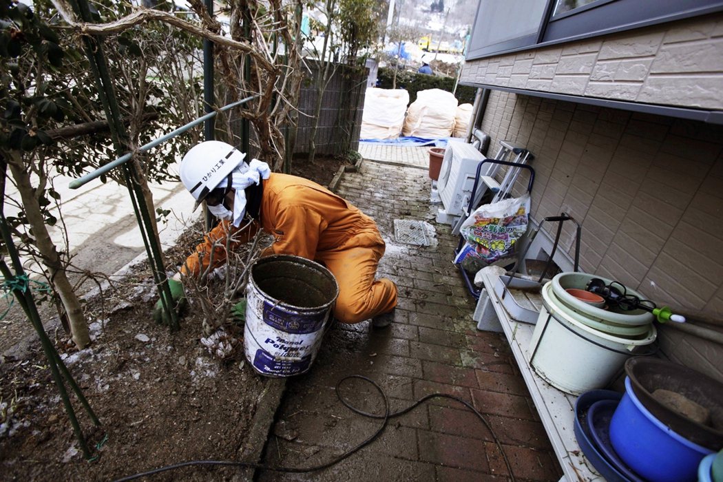 2012年一名輻射除汙工人在剷平民宅外花圃的泥土。 圖／美聯社