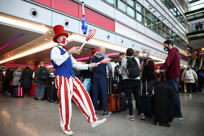 美國八日起對完整接種新冠疫苗的外國旅客重開陸空邊境，英國希斯洛機場出現大批旅客排隊報到準備飛往美國，一名特技演員表演雜耍提供娛樂。（路透）
