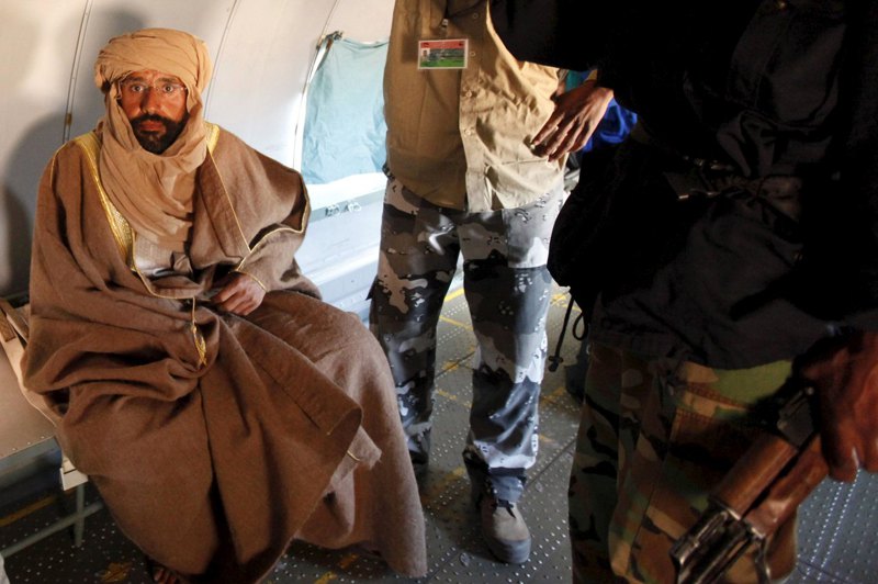 利比亞強人格達費次子薩義夫（左）的人生相當戲劇化，從天之驕子淪落到階下囚，如今復出要選總統。圖為2011年在逃亡途中遭反抗軍捕獲，被送上一架飛機前往辛坦市途中。路透
