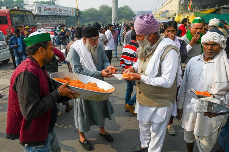 印度總理莫迪19日宣布廢除三條農業法後，北方邦加茲阿巴德市農民在街頭分送甜點慶祝。法新社