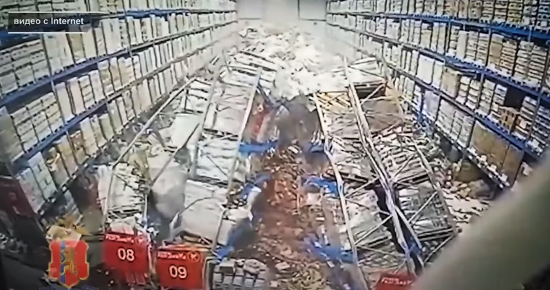 俄罗斯某仓库一排货架突然倒塌，底下的一名员工惊险躲到另一排货架下，未料该货架也接连倒塌，他惨被压在金属架和杂物底下。图撷自(photo:UDN)