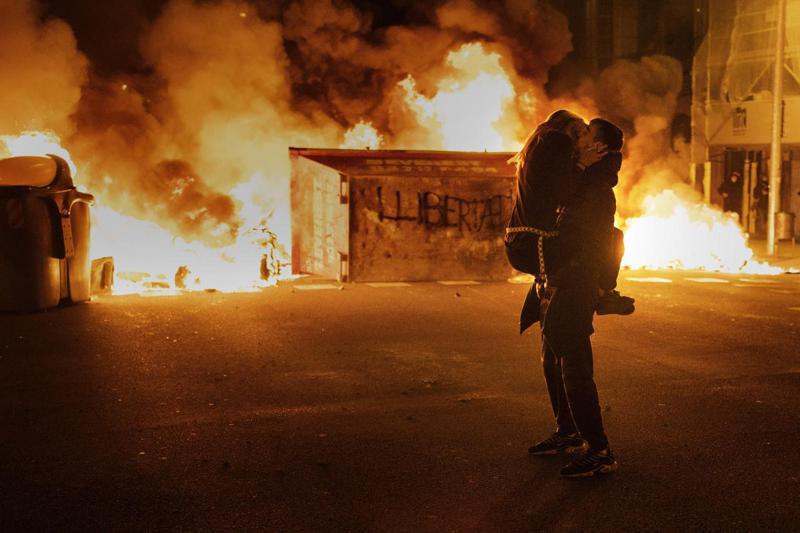 西班牙巴塞隆納一對男女2月18日在熊熊大火前熱情擁吻。西班牙饒舌歌手哈塞爾因侮辱王室被定罪入獄，民眾上街示威抗議當局箝制言論自由，並在與警方衝突時放火焚燒路障。美聯社