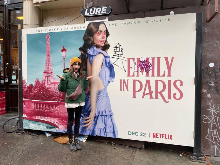 莉莉柯林斯在被亂畫的「艾蜜莉在巴黎」看板前作出目瞪口呆的表情。圖／摘自IG