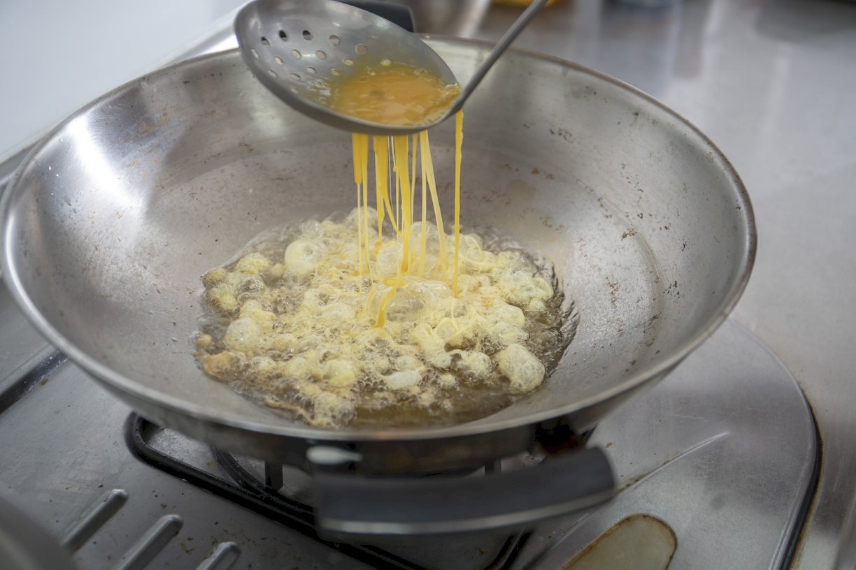熱油鍋後把蛋液從多孔漏勺的上方慢慢倒入，並翻攪約一分鐘。 圖／郭宏軒 攝影