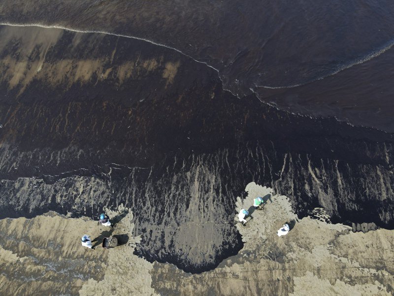 圖為東加火山噴發引起的高浪導致漏油後，工人們正在觀察位於秘魯卡韋羅海灘水域的石油。美聯社