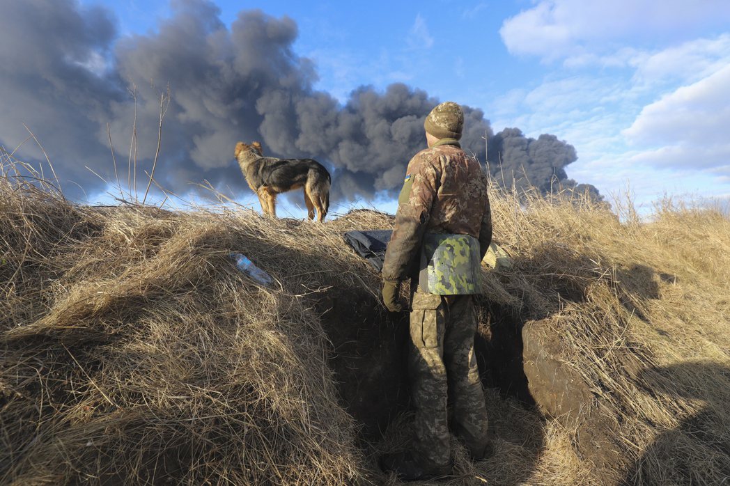 基輔郊區，一名烏軍士兵與他的狗，看著瓦西里基夫儲油槽被俄軍轟炸的爆炸黑煙。 圖／...