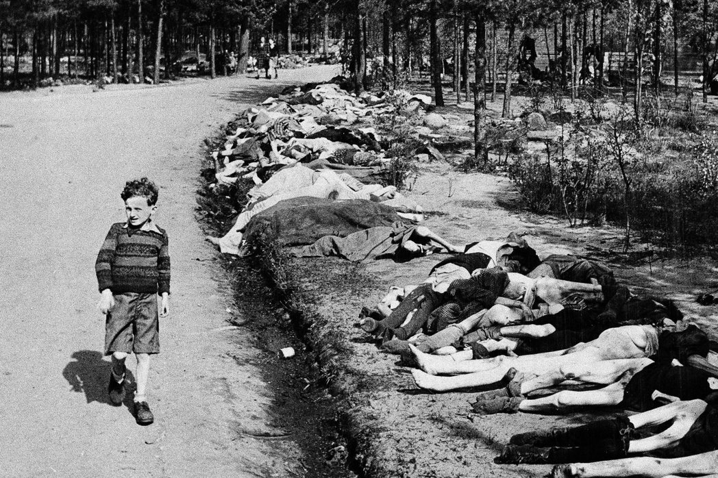 1945年，英國軍隊解放貝爾根集中營後，一名小男孩走過一群罹難者遺體。  圖...