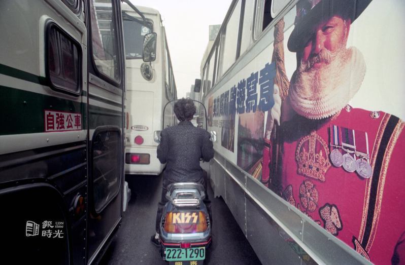 馬路如虎口，一輛小機車穿梭在公車陣中，景象十分危險。日期：1990/2/19。來源：聯合報。攝影：李阿明