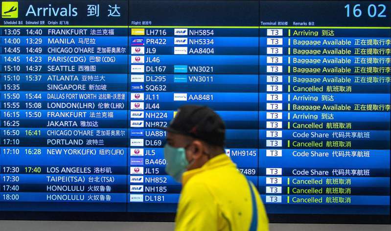 一名今年3月2日旅客經過日本東京羽田國際機場大廳電子航班表。法新社