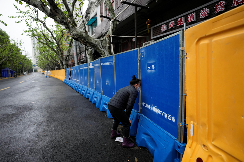 圖為4月中，上海一名婦人試圖向封控區域內的商家買些食物。路透