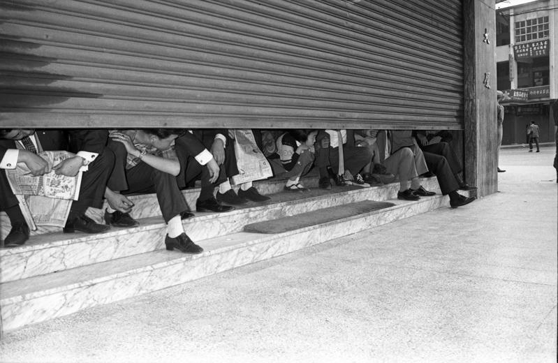 1969年5月7日，台北街頭下午無預警地響起防空警報，民眾配合緊急疏賽到建築物內，由於人數太多室內擠不進去，鐵門沒有完全放下，民眾低頭瞄一眼路上演習的狀況。圖／聯合報系資料照片