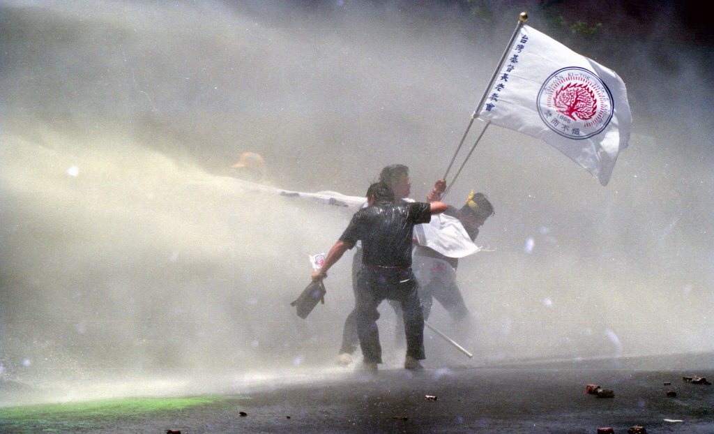 1990年5月29日，五二九反軍人組閣群眾抗議活動，一群手持台灣基督長老教會布條的男子無懼強力水柱噴射，向拒馬衝鋒，帶動群眾拚鬥士氣，逼進拒馬。 圖／聯合報系