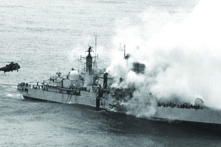 中彈後燃燒中的雪菲爾號，一架海王式在旁支援。注意船身中段縱向的粗黑色帶，是福島戰爭期間，避免與阿根廷海軍同型艦混淆的識別色。圖／取自維基百科