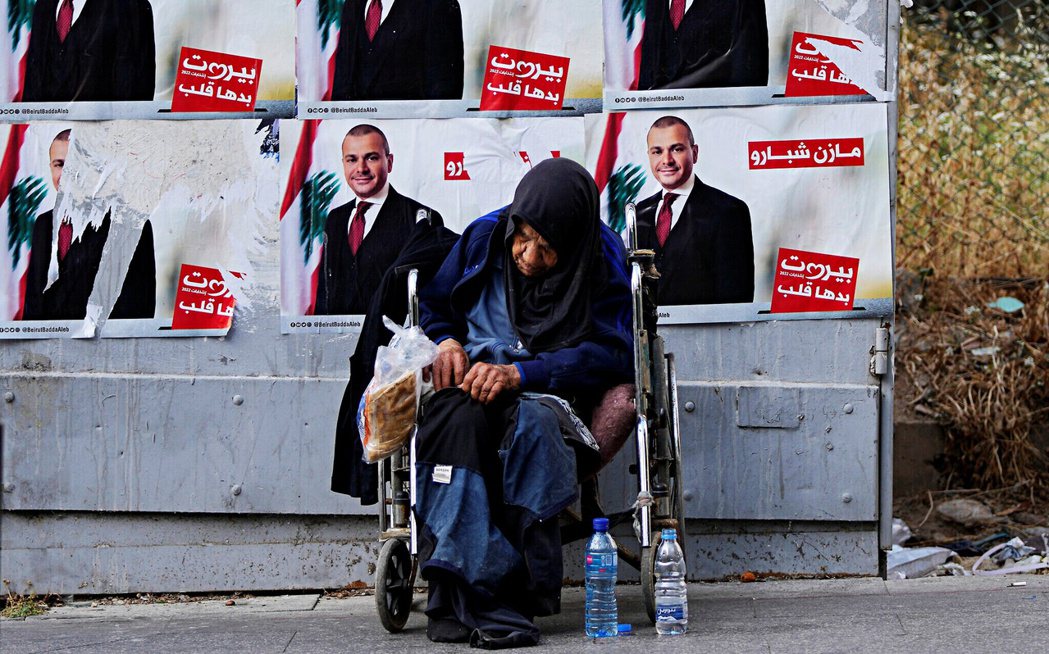 2022年5月，一名無家可歸的婦女坐在貝魯特街頭的國會大選競選海報前。 圖／美聯...