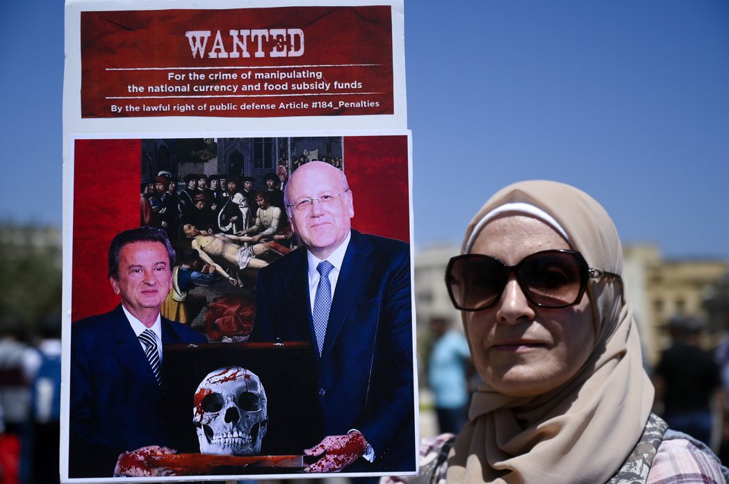 2022年6月，黎巴嫩民眾在貝魯特市抗議活動中，抗爭者舉着一張海報，上面畫着總理...