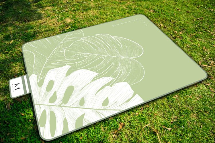 「M One仲夏野餐墊」以簡單線條勾勒出龜背芋圖樣，並使用酪梨綠與米白色打底。單...