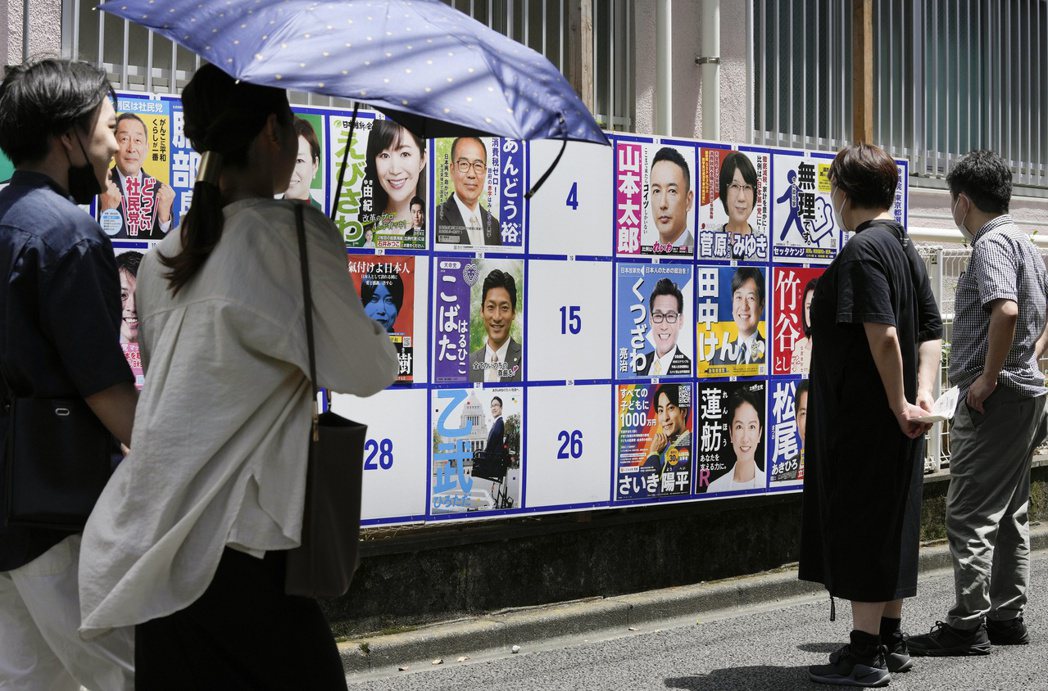 選民在東京的一處投票站外觀看候選人海報。 圖／歐新社