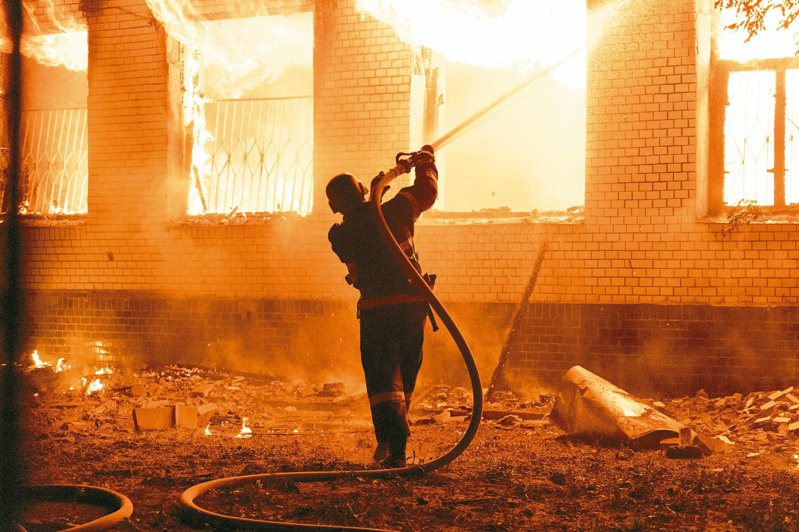 一名消防員一日晚間朝著尼古拉耶夫一間遭俄軍砲擊而起火的醫院建築噴水。（路透）