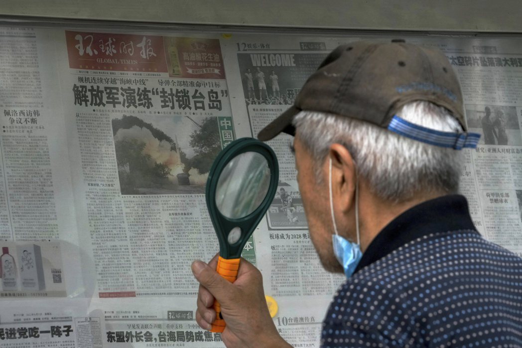 2022年8月7日，在北京一名男子使用放大鏡閱讀有關中國人民解放軍進行軍事演習的...
