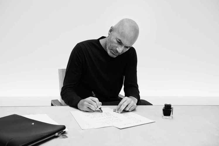 Zinédine Zidane在黑白行形象中不僅執持萬寶龍經典皮件，同時低頭書寫...
