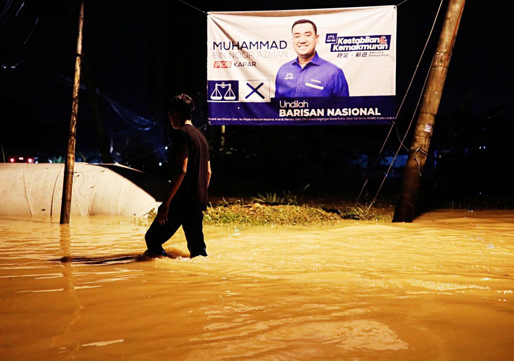  圖為11月10日淹水的雪蘭莪，一位男生經過競選的橫幅海報。 圖／路透社