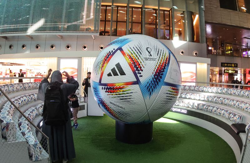 旅客10日在卡達首都多哈國際機場新中央大廳觀看巨大足球擺設。法新社
