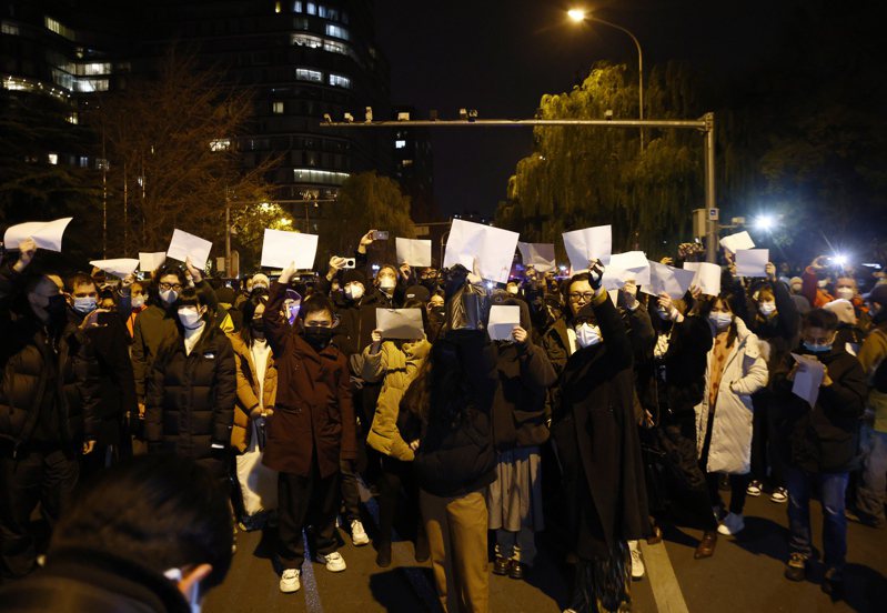 北京27日晚的「白紙運動」，多人舉白紙到亮馬橋悼念新疆死者。（歐新社）