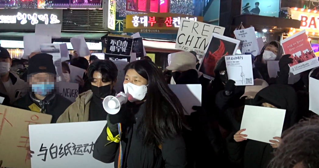 手持擴音器的南韓市民聲援抗議的中國留學生，並用南韓過去的歷史事件同理白紙革命的處...