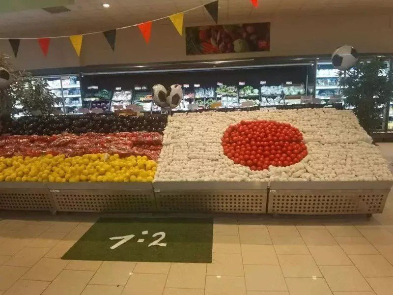 臉書粉專「野腳小秋」近日分享一間德國連鎖超市生鮮區的照片，左邊用黑、紅、黃3色食物擺成德國國旗，右邊則用紅色番茄與白色蒜頭擺成了日本國旗，但地板放的地墊上面寫「1：2」，讓大家笑翻。(圖／臉書)