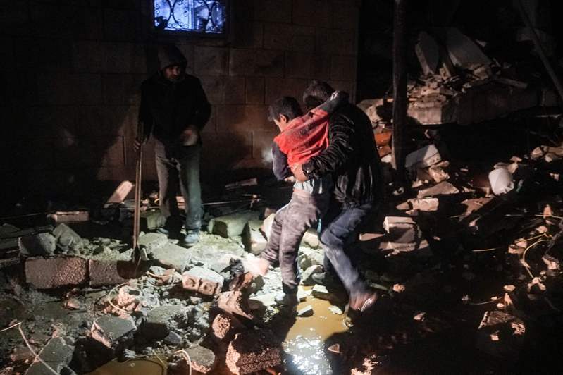 敘利亞西北部阿夫林一名男子6日抱著一名受傷孩童離開被強震震垮的房舍。法新社