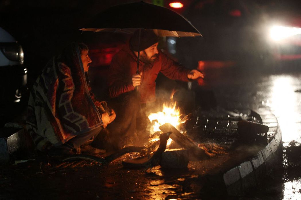 土耳其卡赫拉曼馬拉什省的災民，在雨夜中烤火取暖。 圖／法新社