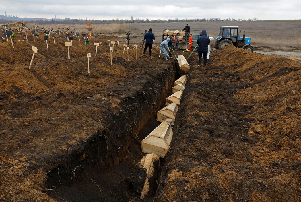 2023年2月4日，烏克蘭南部馬立波的工人將一具又一具棺木放入公墓墓穴。 圖／路...