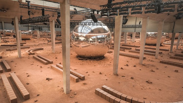 Off-White大秀現場中央有一個巨型金屬球體，座落在像是月球表面般的土壤中，...