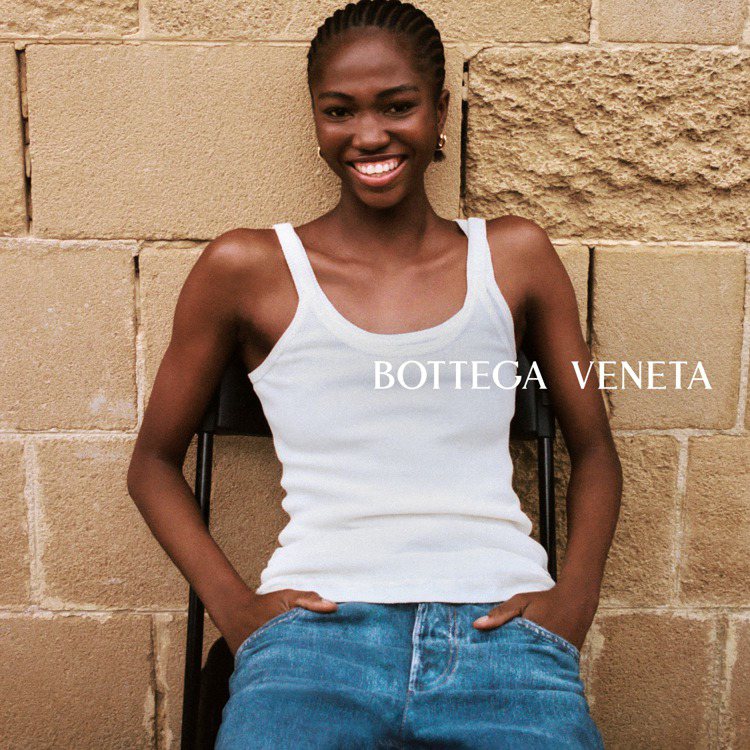 在Bottega Veneta的春夏形象廣告中，模特兒時而在海岸邊赤腳而立、或背對鏡頭書展雙臂，也有人穿著白色背心、牛仔褲坐在石牆前露出自信笑容。圖／Bottega Veneta提供