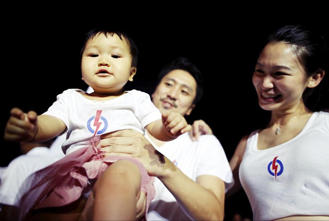 图为身穿新加坡执政党人民行动党(PAP)标志衣服的父母。图／路透社
