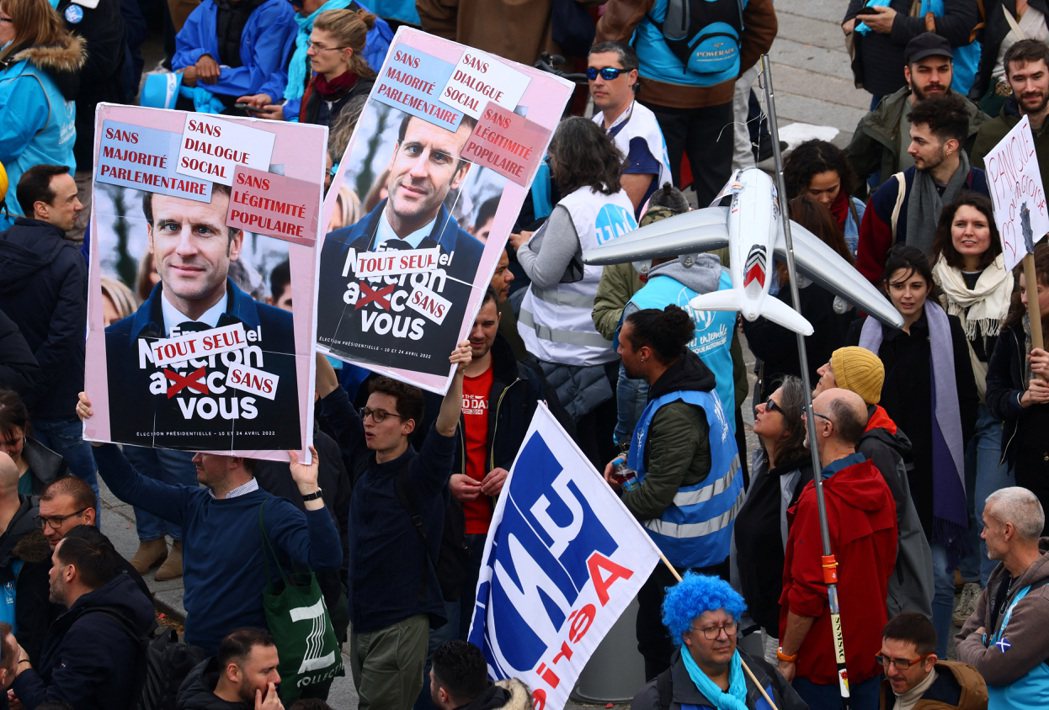 法國巴黎反年改抗議民眾23日舉著有總統馬克宏肖像的標語牌抗議。路透
